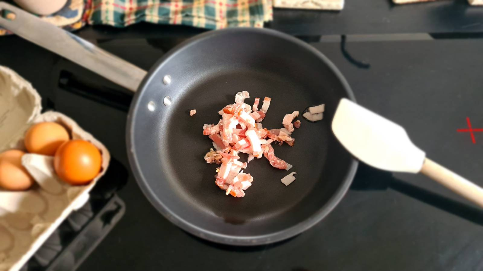 Boczek z cebulą na patelni, łopatka kuchenna, jajka w skorupkach